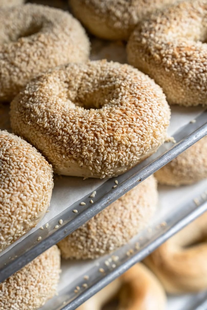 Freshly baked sesame bagels on a metal baking tray, ready to be served.