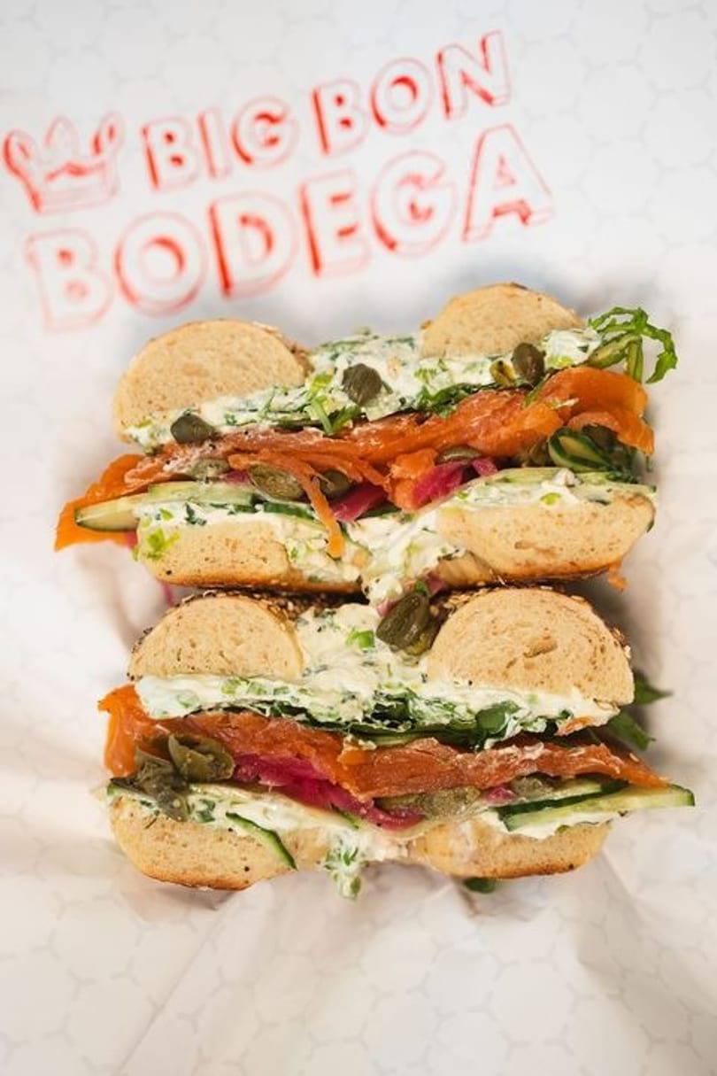 Two bagels with smoked salmon, cream cheese, capers, and cucumber on Big Bon Bodega paper.