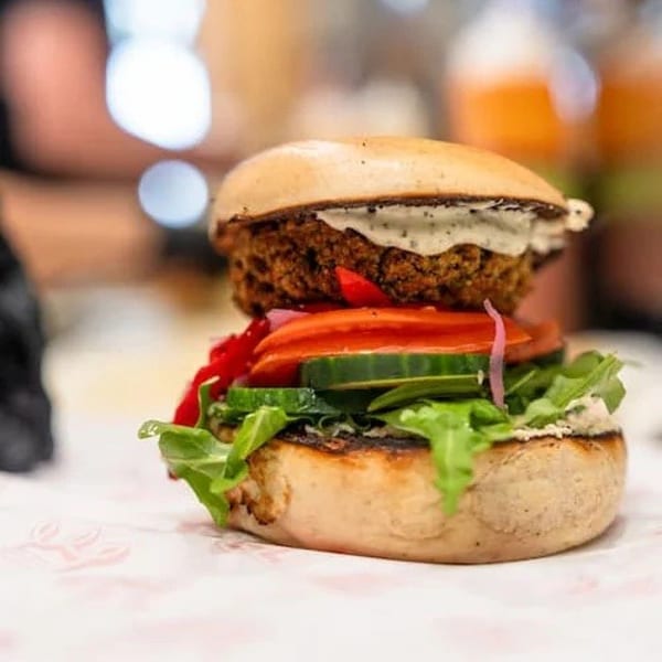 Close-up of a veggie burger with a thick patty, lettuce, tomato, cucumber, and sauce.