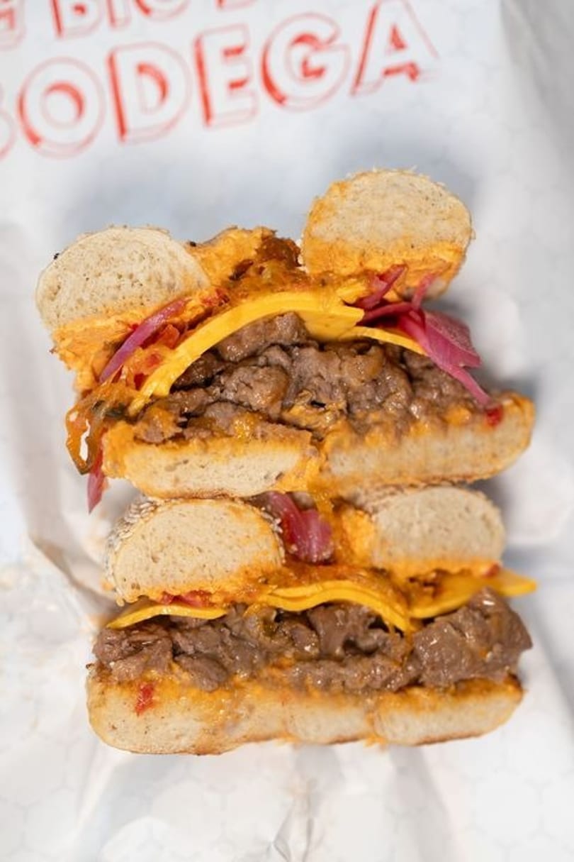 A Mickey Mouse-shaped bagel sandwich with steak, melted cheese, and pickled onions.