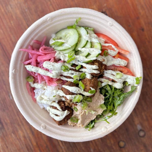 Falafel bowl with rice, pickled onions, cucumbers, tomatoes, hummus, and green sauce.