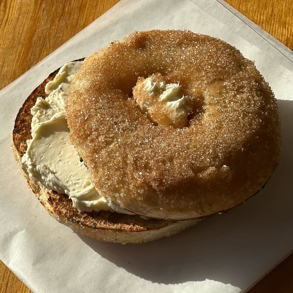 Sugar-coated bagel sandwich filled with thick cream cheese on parchment paper atop a wooden table.
